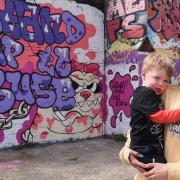 Megan Campbell, victim of domestic abuse, with her two-year-old son, Stanley, by the graffiti 'Stand Up To Abuse' she has painted highlighting Leeway, near Anglia Square. Picture: DENISE BRADLEY